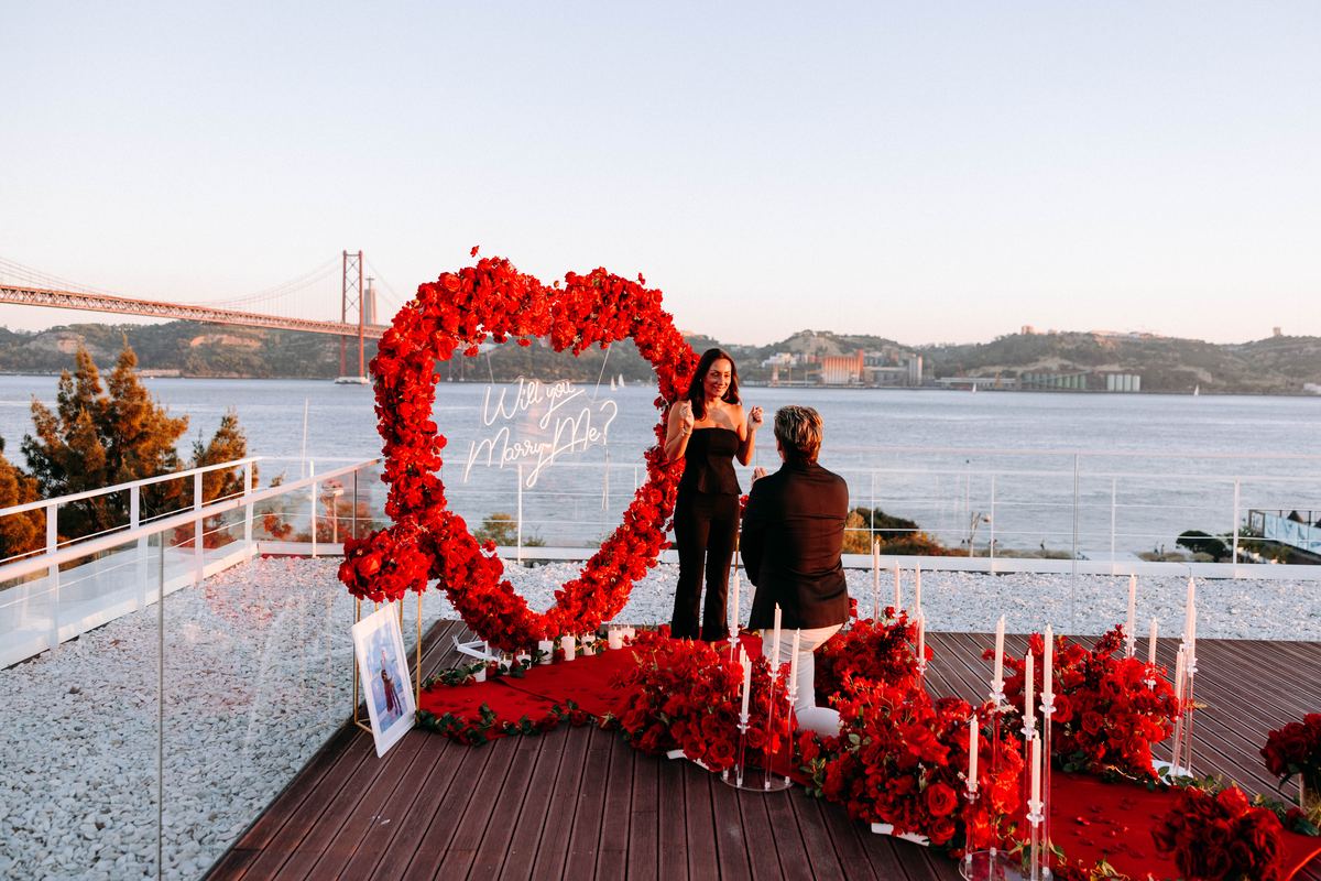 Marriage proposal in Lisbon – red flower heart decoration with iconic bridge at sunset
