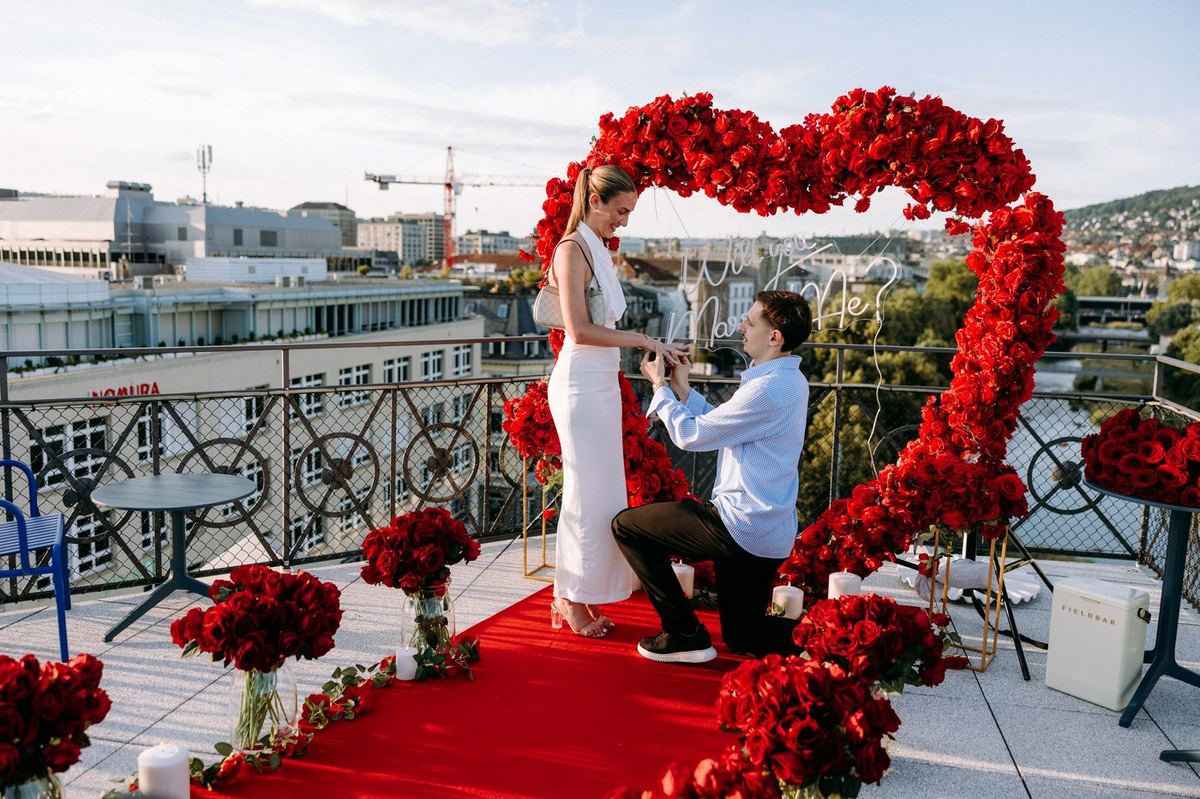 Marriage proposal in Zurich – rooftop red heart with neon sign, man kneeling with ring