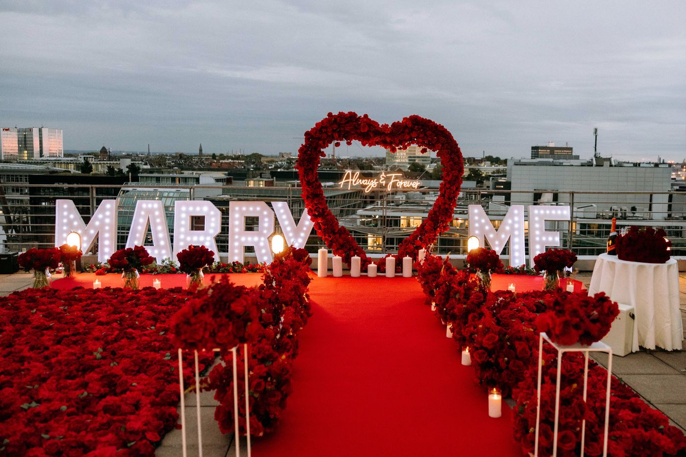 Shine Bright rooftop proposal – illuminated MARRY ME sign surrounded by red roses