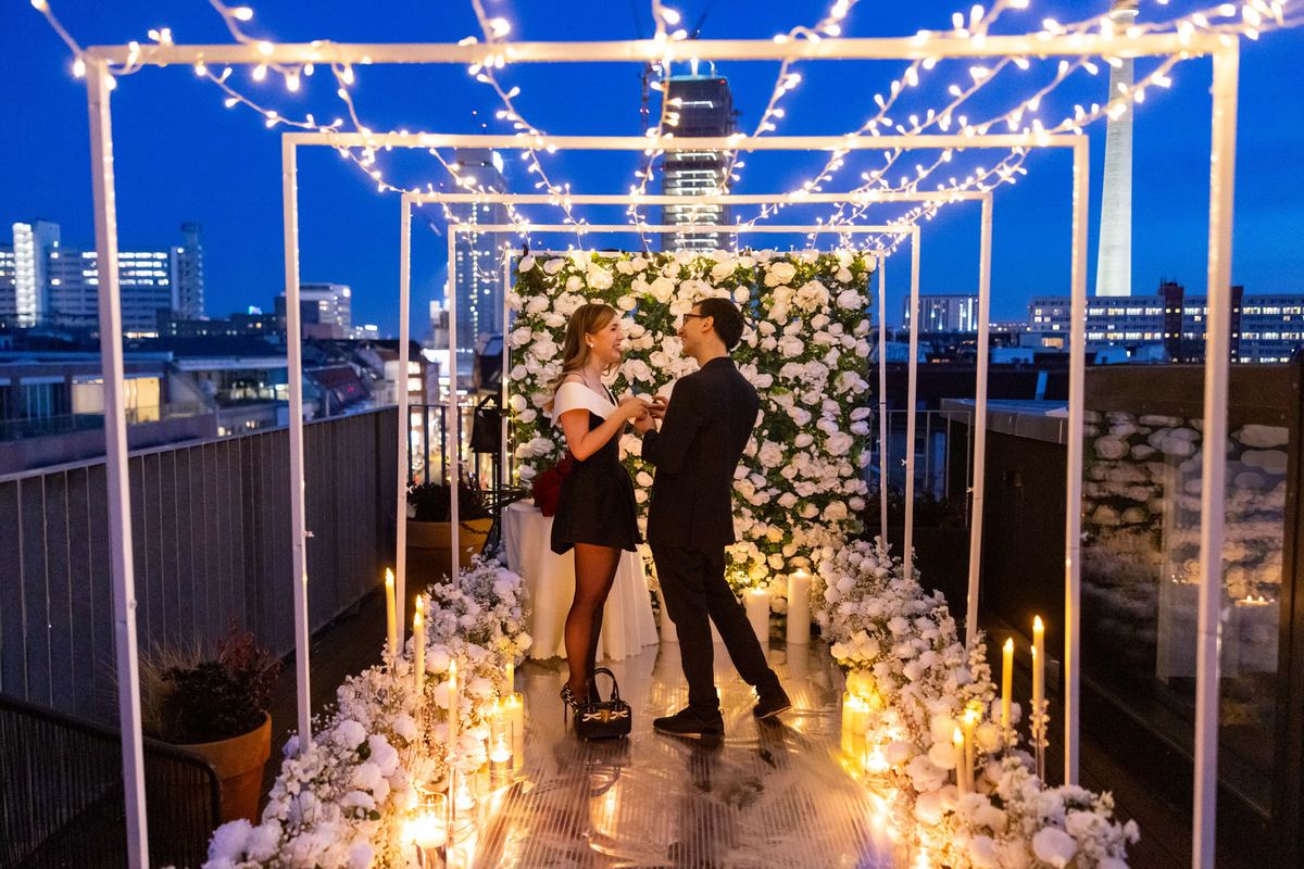 Marriage proposal in Berlin – rooftop with white flower wall, fairy lights and couple at night