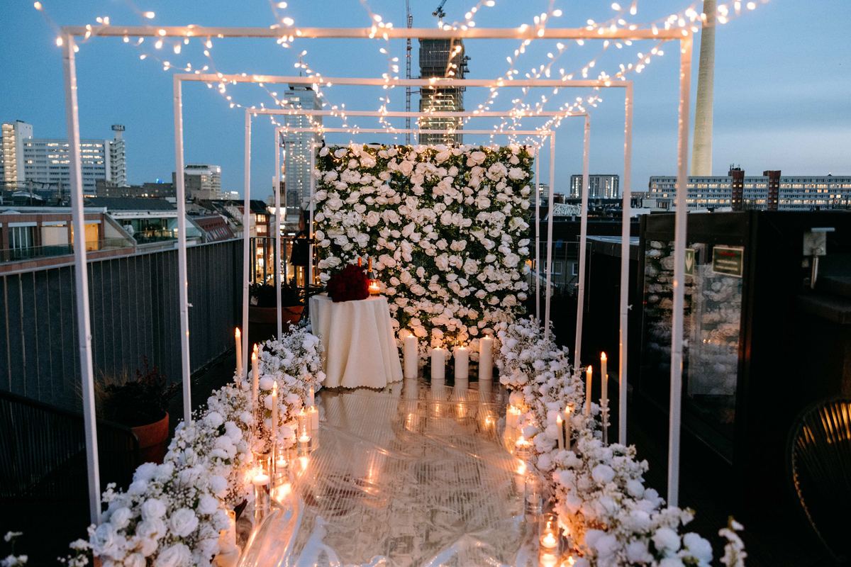 Marriage proposal in Berlin – rooftop white flower wall with romantic fairy lights tunnel