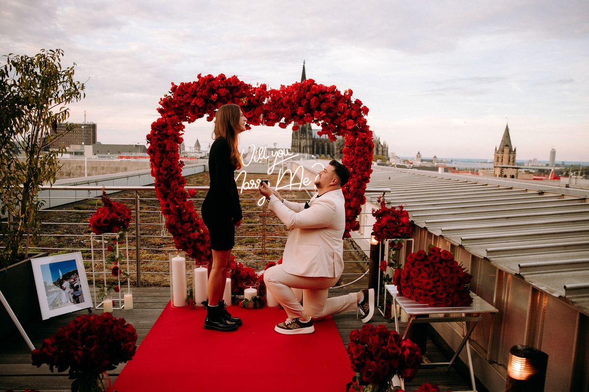 Marriage proposal in Cologne – cathedral rooftop with red flower heart, man kneeling with ring