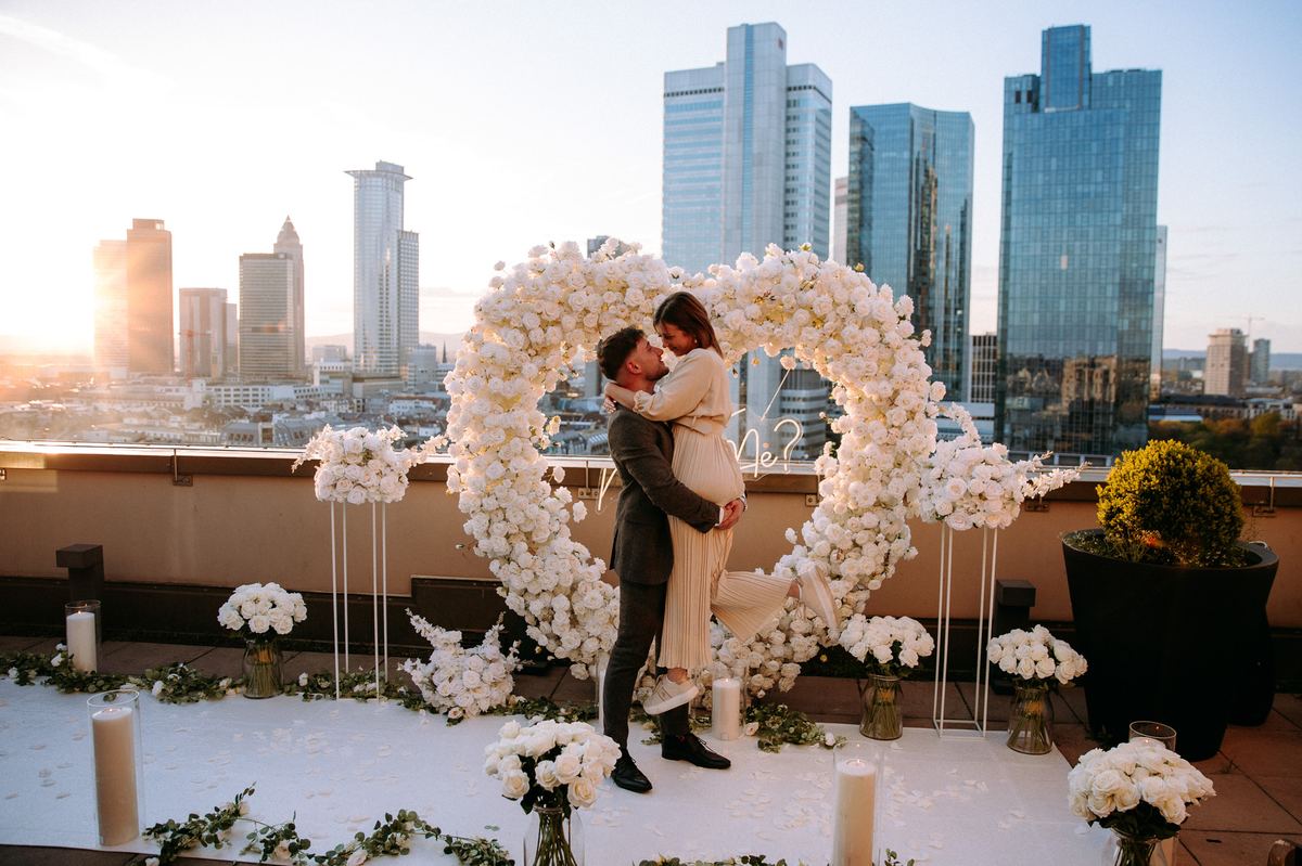 Marriage proposal in Frankfurt – skyline rooftop with white heart, couple kissing at sunset