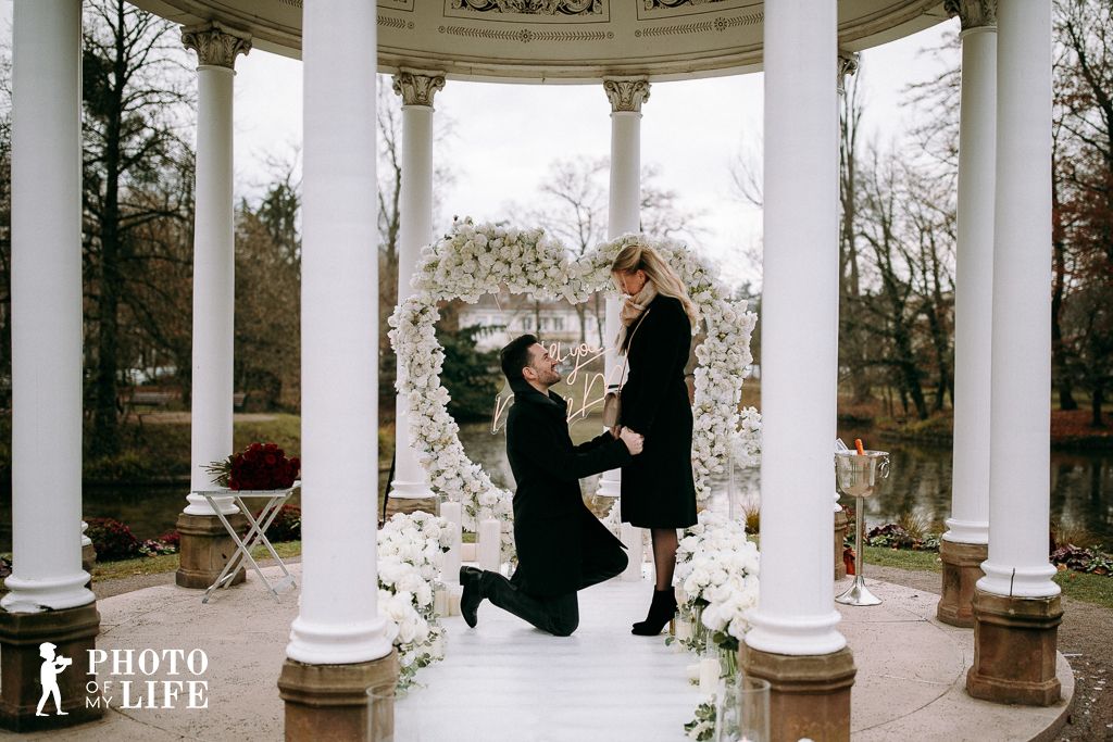 White Elegance proposal in park pavilion – man kneeling with white flower arch